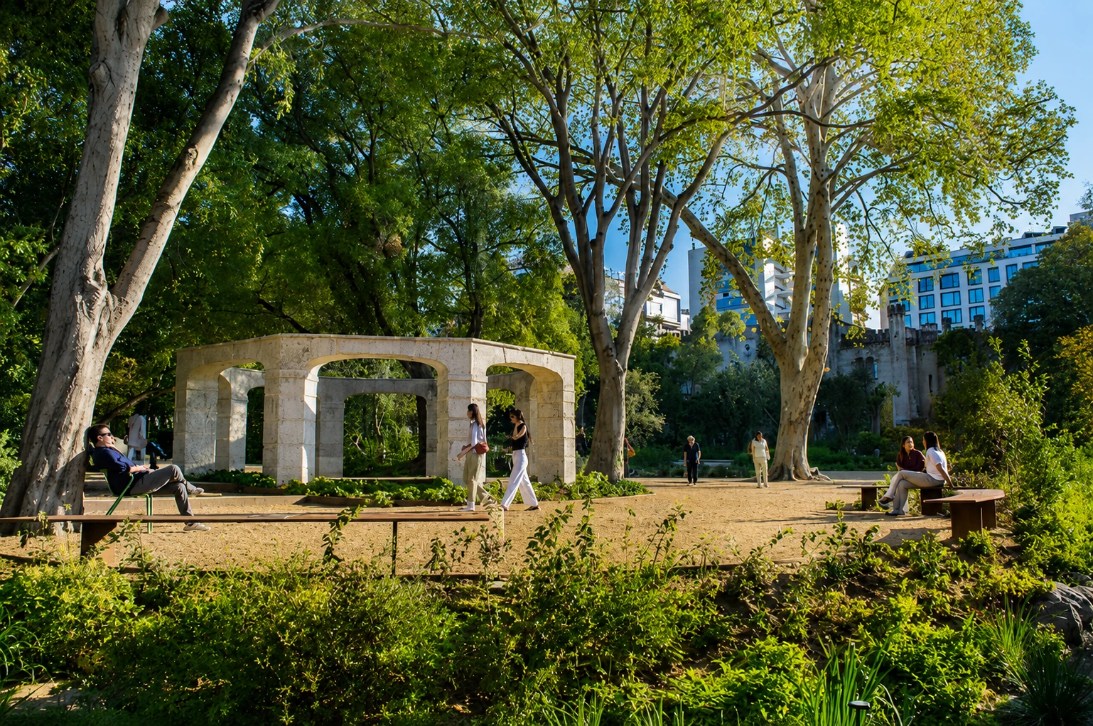 Jardim com arco em pedra, árvores maduras e pessoas em uso do espaço, Avenidas Novas